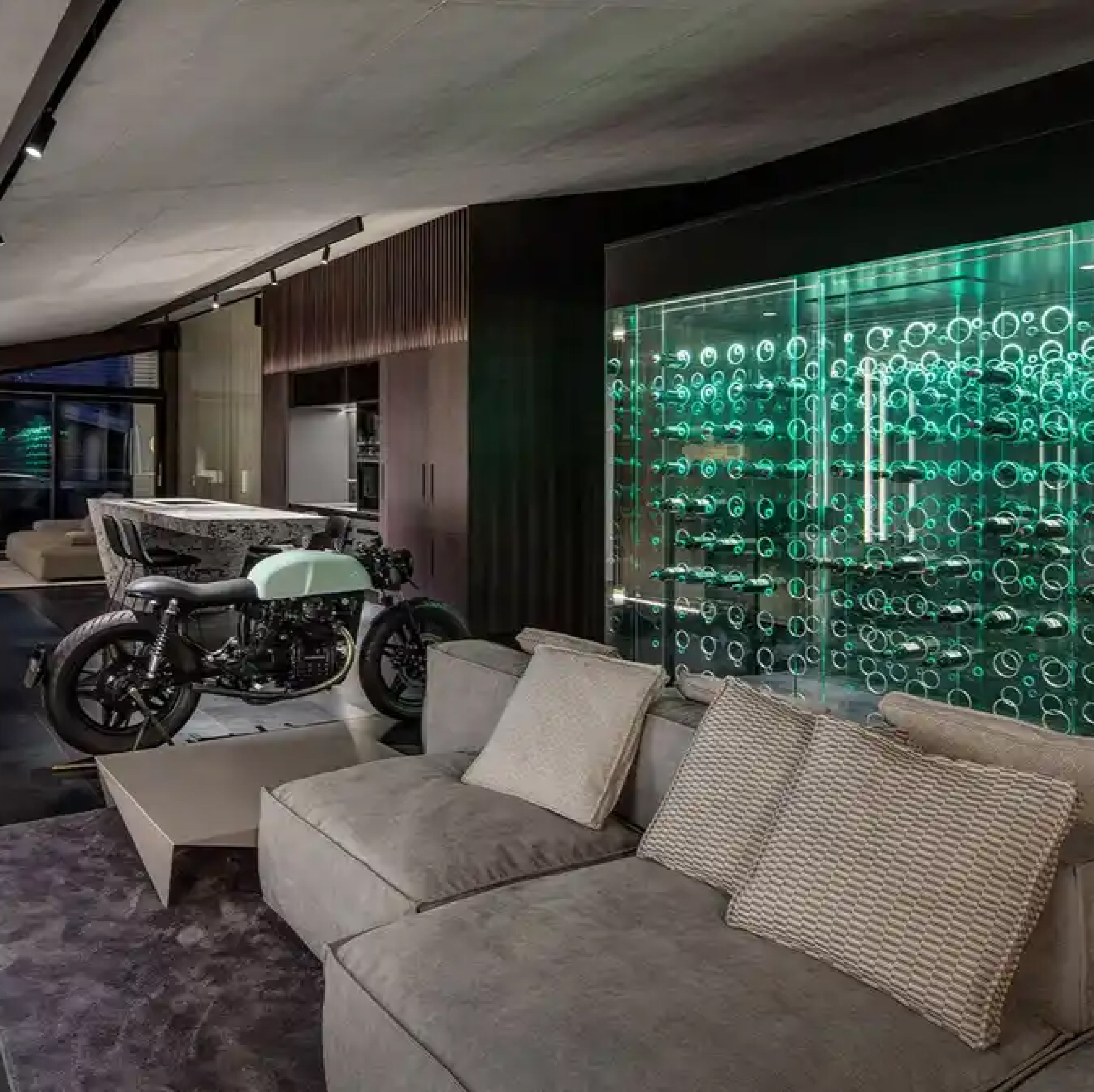 Modern Prague apartment interior with a dark timber kitchen, concrete ceilings, a glowing green wine wall, and a vintage motorcycle.