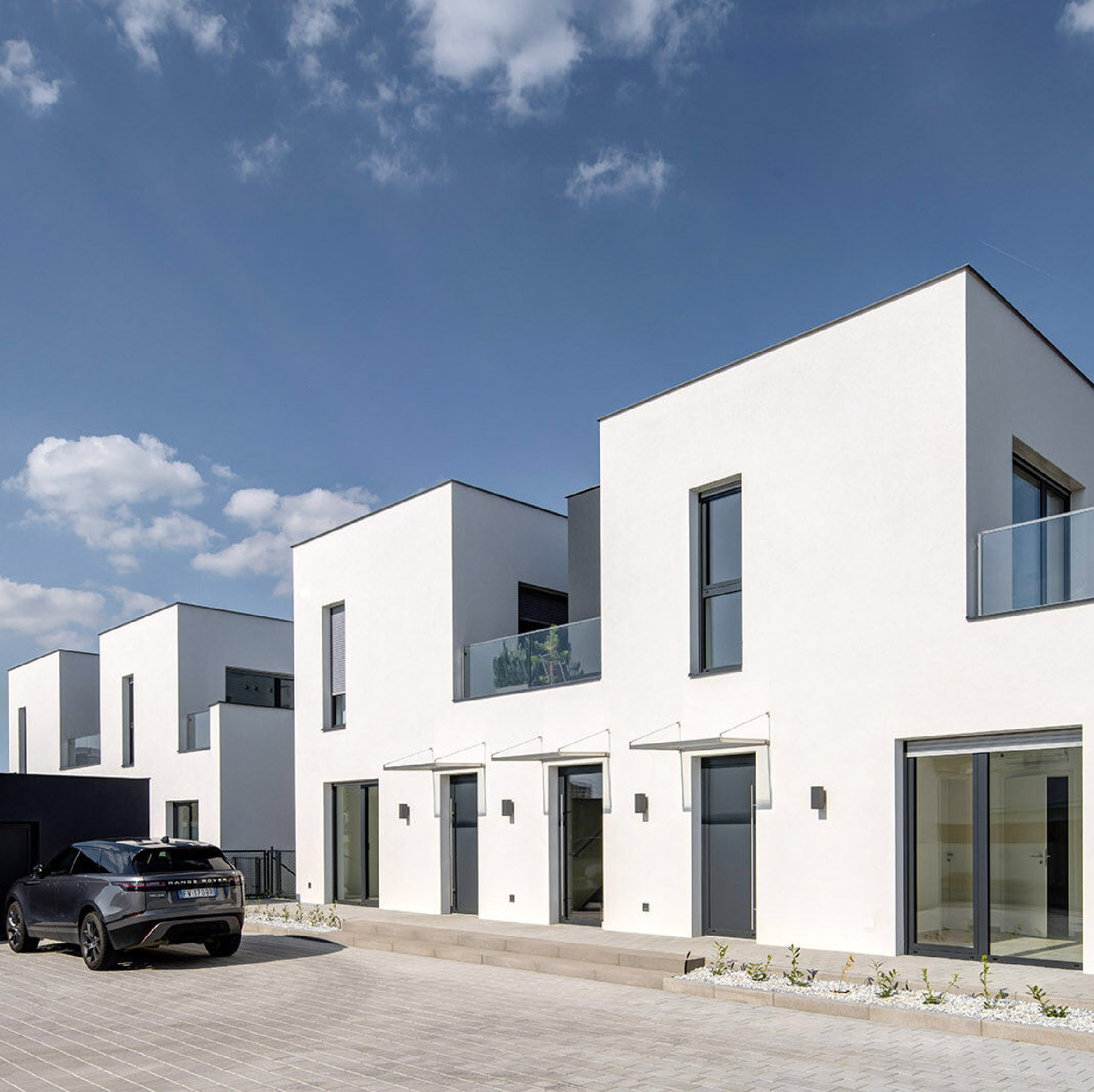 4 Houses by Archicraft, featuring a row of contemporary two-story homes with white facades, dark grey window frames, glass balcony railings, and minimalist entrances beneath slim glass canopies.